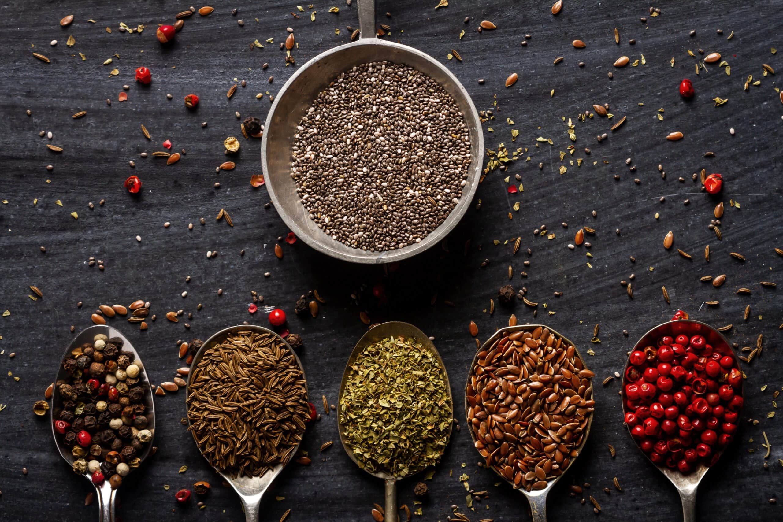 Old,spoons,with,various,seeds,,herbs,and,spices,on,black